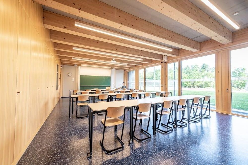 Heller Klassenraum mit Holzträgern und bodentiefen Fenstern